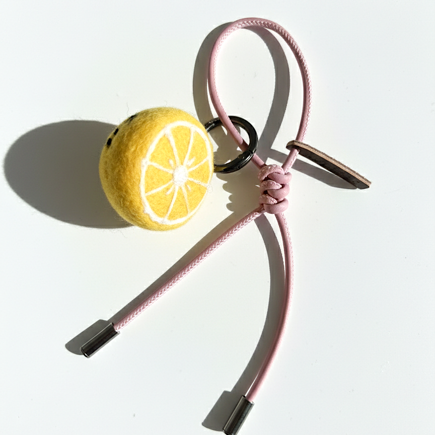Needle-felted lemon slice bag charm with pink cord and silver aglets.