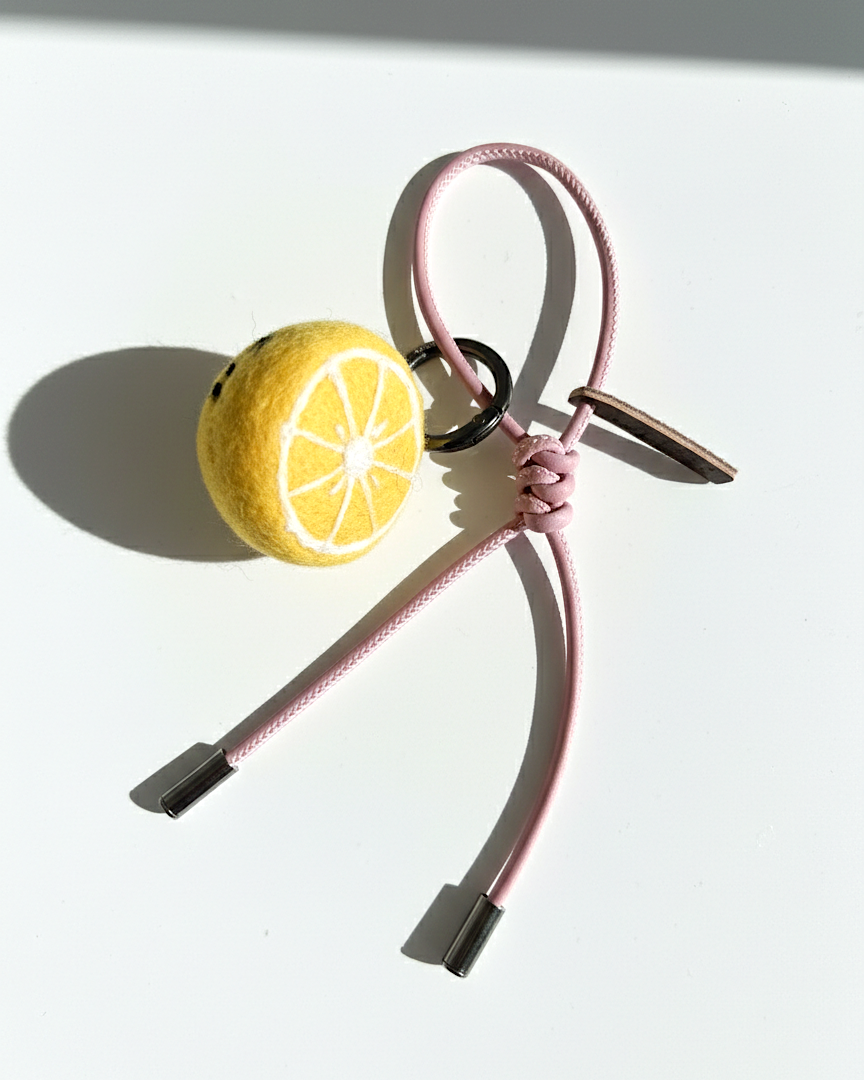 Needle-felted lemon slice bag charm with pink cord and silver aglets.