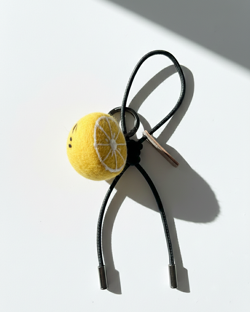Artisan felted lemon slice accessory with black leather cord and silver hardware.