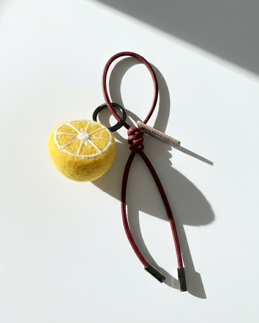 Miniature needle-felted lemon slice keychain with dark red burgundy cord.