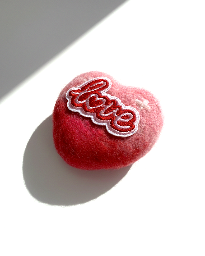 Close-up of a decorative wool felt heart magnet showing the fuzzy texture of the finest Merino wool and an artistic red-to-pink ombre finish.