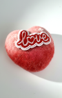 A soft-focus shot of a handmade needle-felted heart gift featuring a "Love" patch, perfect for Valentine's Day or romantic home decor.