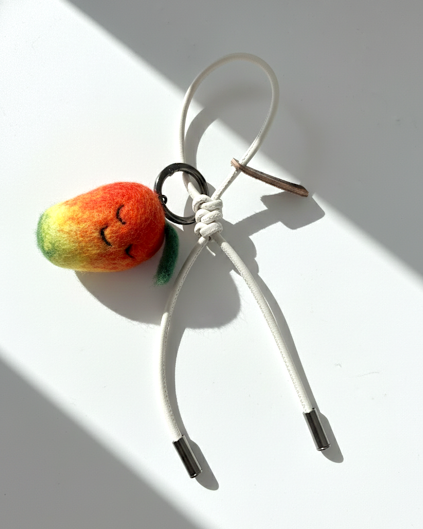 Handmade smiley face mango felt charm with cream white cord and metal tips.