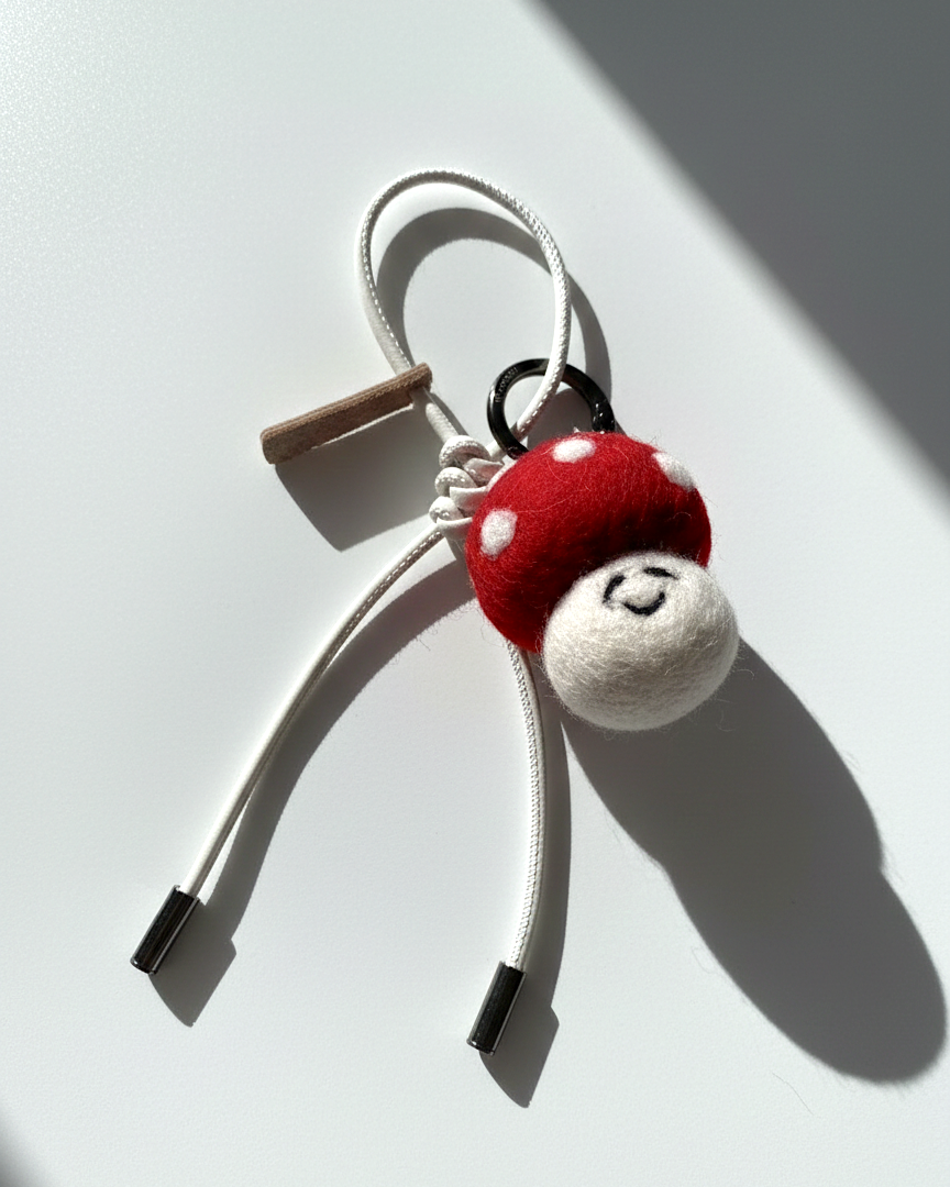 Artisan felted red toadstool keychain accessory with a cream white cord and metal tips.