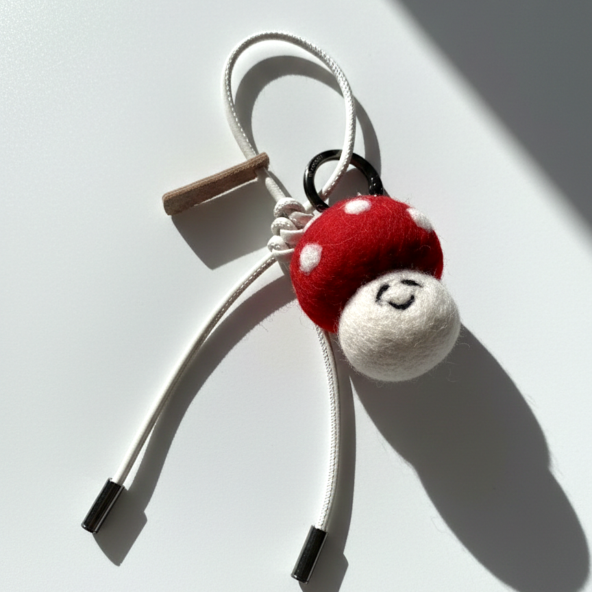 Artisan felted red toadstool keychain accessory with a cream white cord and metal tips.