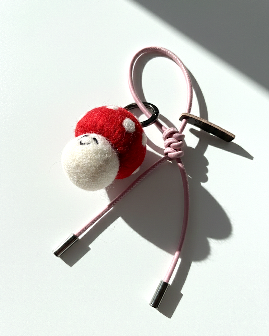 Handmade needle-felted red mushroom bag charm with a light pink cord and silver aglets.