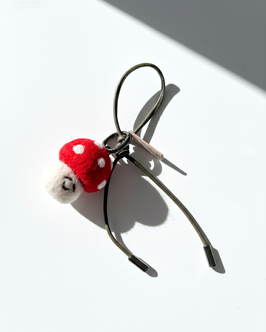 Handcrafted needle-felted toadstool accessory featuring an olive green cord and leather brand tag.