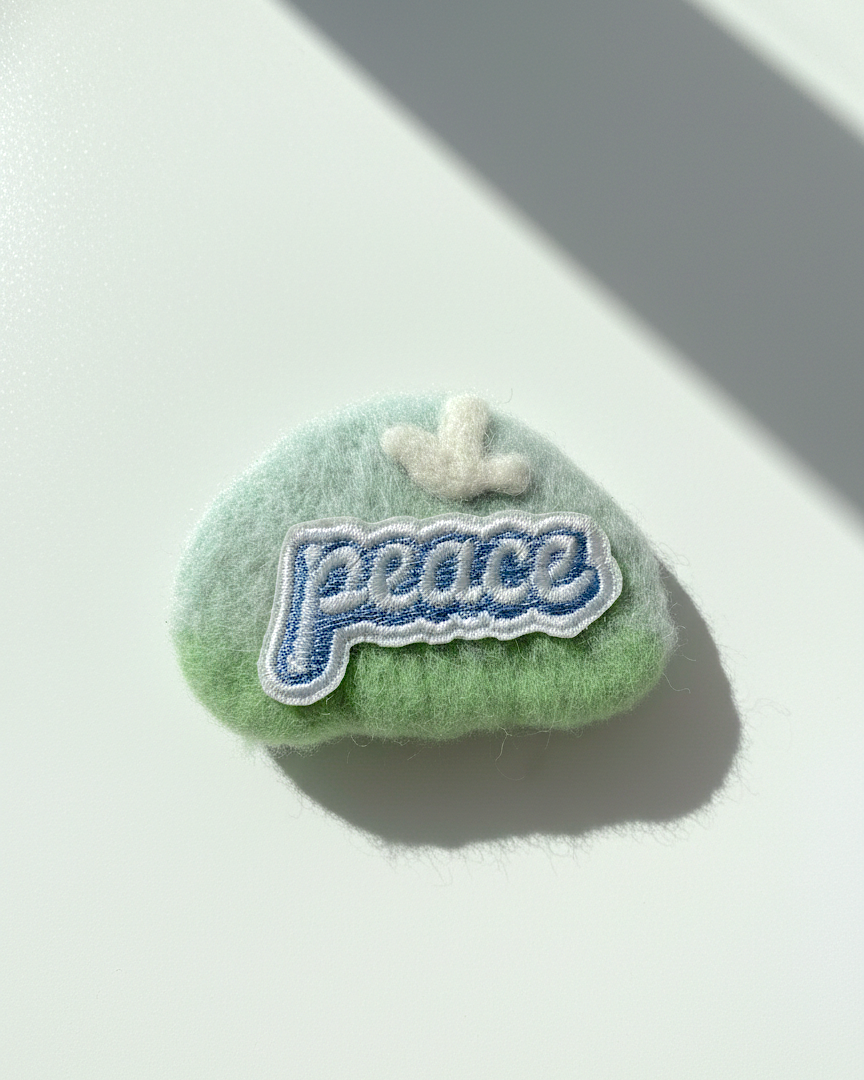 Handmade green wool fridge magnet with embroidered Peace patch and cloud detail, needle-felted merino wool
