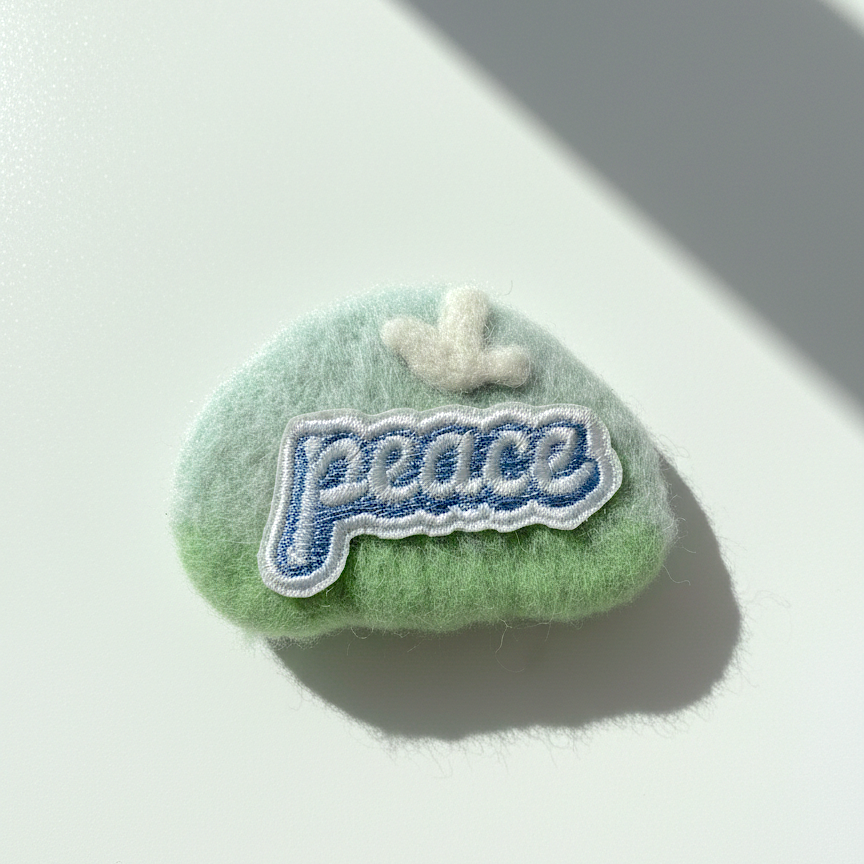 Handmade green wool fridge magnet with embroidered Peace patch and cloud detail, needle-felted merino wool