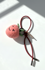 Handmade wool felt strawberry charm with smiling face and red leather loop strap, needle felt fruit bag charm on white background with natural sunlight shadows