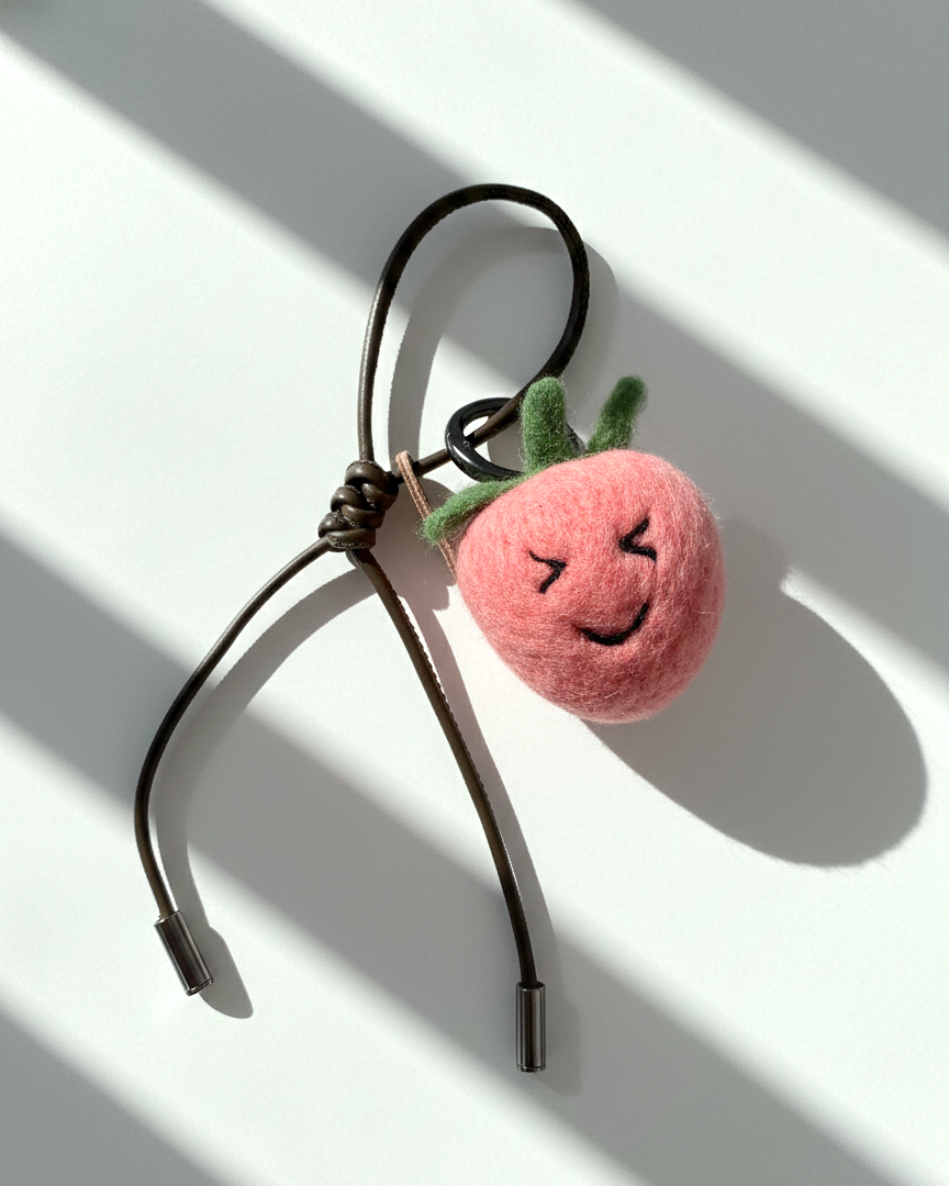 Cute wool felt strawberry keychain with olive leather loop and embroidered face, artisan needle felt fruit charm in soft natural lighting