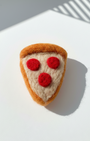 Handmade wool pizza slice fridge magnet with red felt pepperoni details on white surface