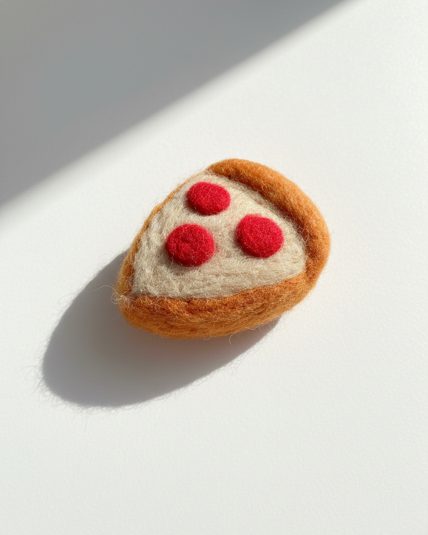 Needle-felted wool pepperoni pizza slice magnet shown at an angle with natural light and shadow