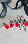 Panning video showing the full color collection of needle-felted strawberry bag charms with four leather strap options: white, pink, black, and red, arranged on a marble surface.