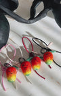 Panning video showing the full collection of needle-felted mango bag charms with four leather strap options: white, black, red, and pink, arranged on a marble surface.