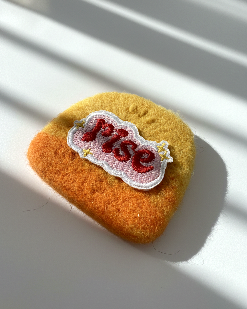 Yellow to orange needle-felted wool magnet with stitched Rise patch, soft rounded handmade fridge decor