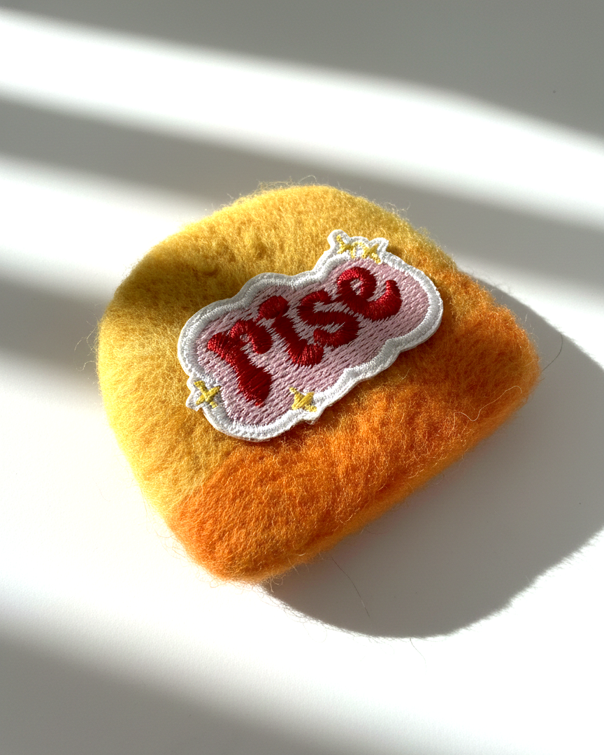Handcrafted merino wool fridge magnet featuring Rise embroidery patch, warm felt texture detail