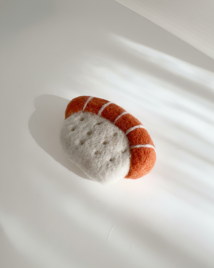Small handmade wool sushi magnet, needle felted salmon nigiri on white background