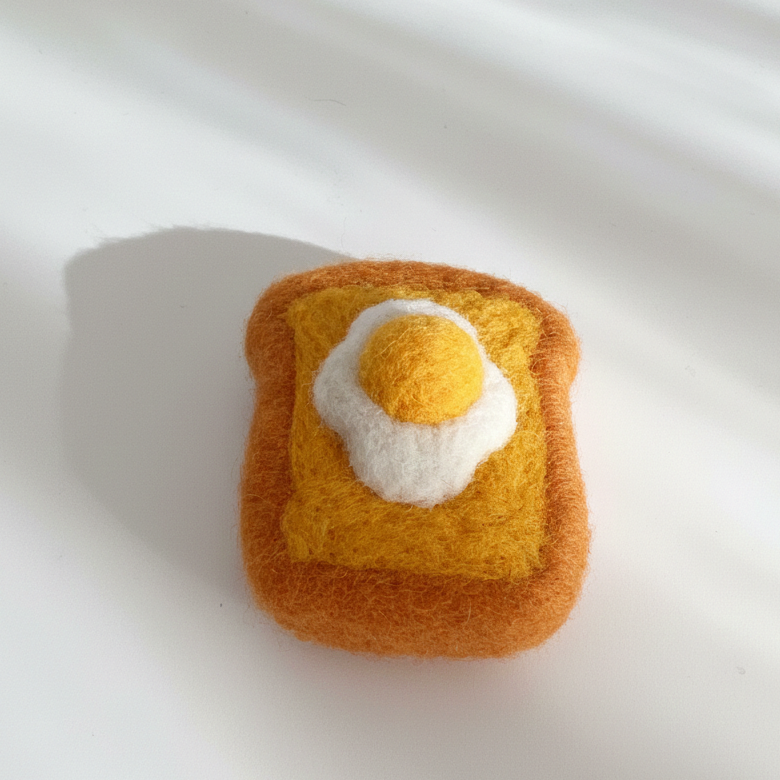 Handmade wool egg toast magnet with fried egg design, photographed in natural light