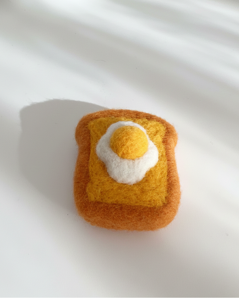 Handmade wool egg toast magnet with fried egg design, photographed in natural light