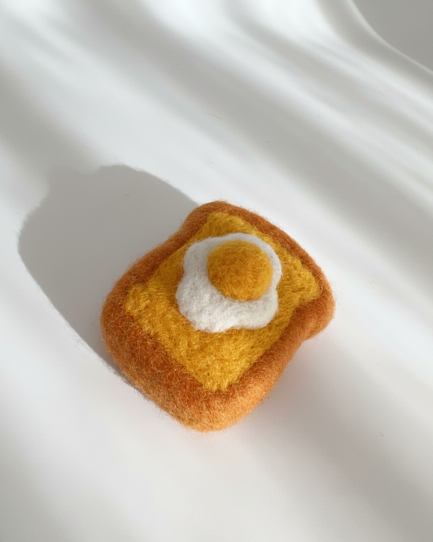 Needle-felted wool egg toast magnet shown from above with soft felt texture